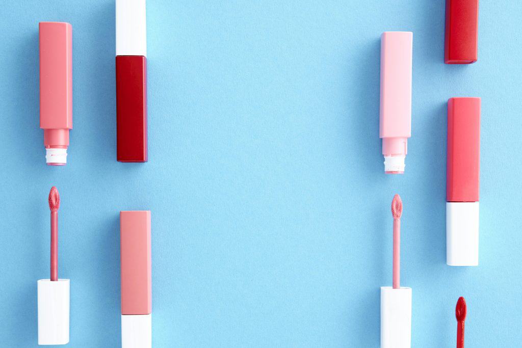 Colorful lip gloss tubes laid out on a bright blue background, showcasing modern cosmetics.